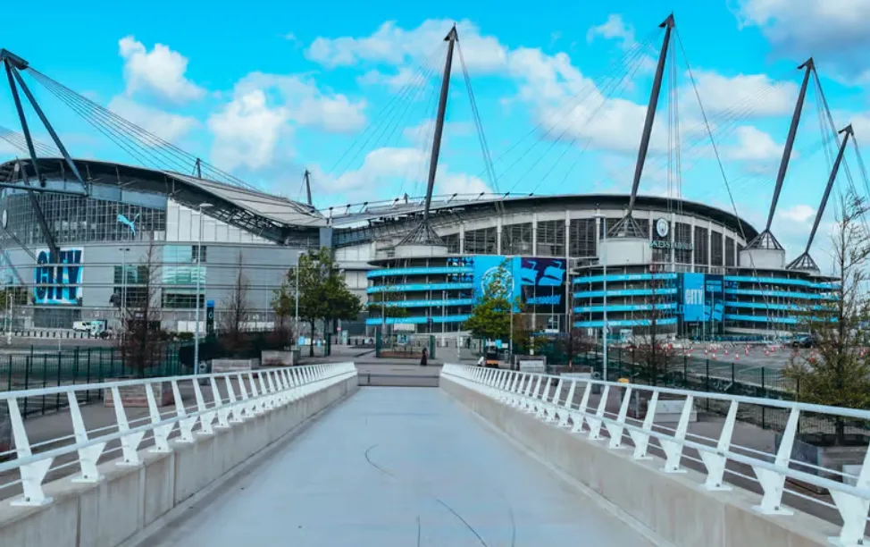 Juma Bah in Manchester City training kit, with the Etihad Stadium in the background.